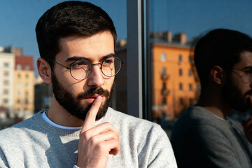 Thoughtful Young Man Wearing Glasses Pondering Outside Building Reflection