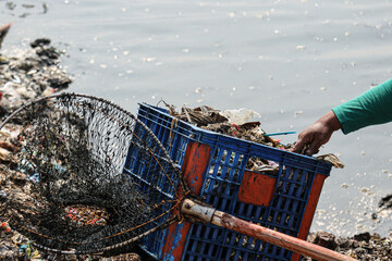 A cleaning officer picks up trash that has washed up on the shore of a pier.