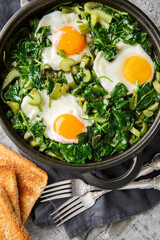 Healthy green shakshuka with eggs, spinach, celery, onion, green pepper and herbs close-up in a frying pan on the table. Vertical top view from above
