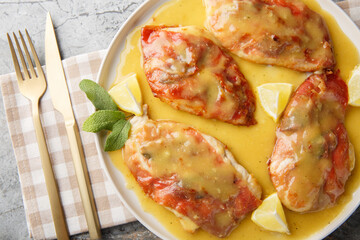 Saltimbocca chicken cutlets topped with prosciutto and sage leaves are pan-seared, then served in a simple white wine butter sauce closeup on the plate on the table. Horizontal top view from above