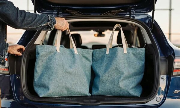 Man loading reusable shopping bags into the trunk of a modern blue car for travel