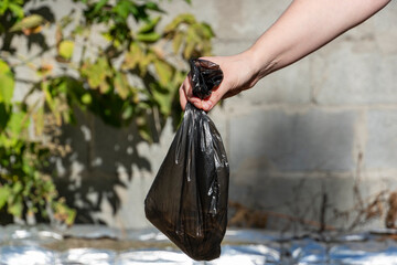 Close up of a hand holding a dog poo inside a plastic bag in a park, concept of responsible pet care, cleanliness, and environmental hygiene. © Nestudio