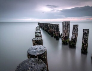 A wooden breakwater at grey misty dawn in a still sea, long exposure 