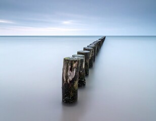 A wooden breakwater at grey misty dawn in a still sea, long exposure 