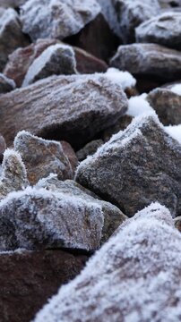 Many natural stones covered with frost on a cold winter day. Close-up texture of frozen stones. Winter background with icy surface.