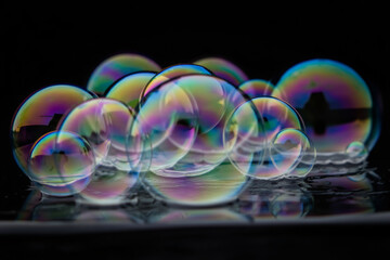 Iridescent soap bubbles cluster on a black background with glittering hues.