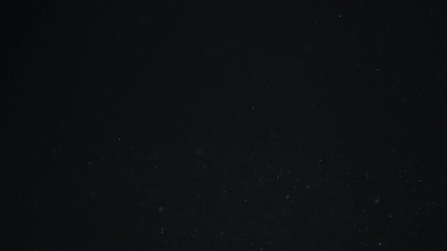 Slow motion rack focuso f dust particles float in sunlight on black background