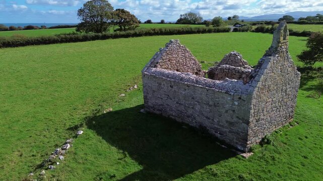 Lligwy chapel aerial view slow circling lush meadow farmland medieval churchyard ruins close up