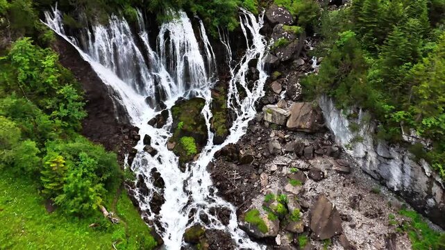 Cascading waterfall at Sibenf&auml;lle in Lenk, Switzerland, flowing over mossy rocks and rugged terrain surrounded by lush green forest and steep cliffs, creating a striking alpine natural landscape