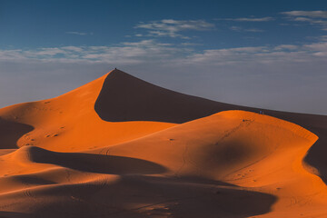Golden dunes of the Sahara Desert in Morocco at sunset – scenic sand landscape with waves of dunes and dramatic light in North Africa