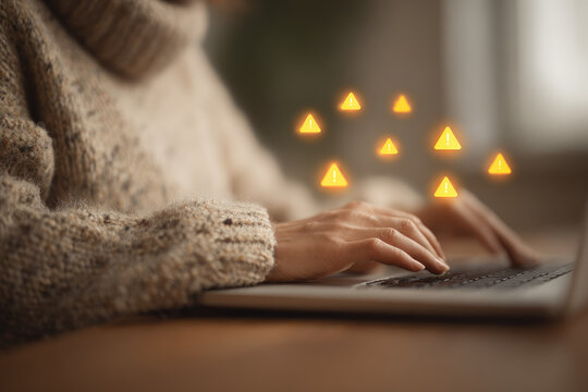 Woman hand typing on laptop with warning icons cozy sweater digital security alert home office warm lighting cyber threat technology risk online safety autumn mood focused expression