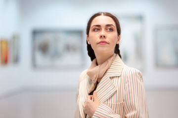 Portrait of young Caucasian woman in elegant jacket contemplating in the modern art gallery. Concept of cultural education and Museum Day