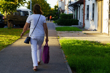 Woman walking on a sidewalk in warm evening light while carrying a purple bag