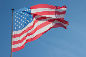 Vibrant American flag waving in the breeze against a clear blue sky, showcasing its iconic red,...