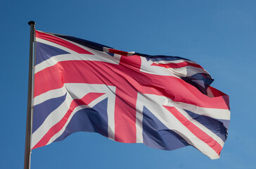 Flag of the United Kingdom waving in the wind against a clear blue sky, symbolizing national pride...