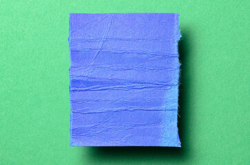 One single blue torn ripped wrinkled crumpled blank paper note with shadow and copy space for text on green background