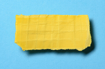 One single yellow torn ripped wrinkled crumpled blank paper note with shadow and copy space for text on light blue background