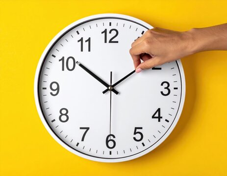 Hand adjusting a white clock on a yellow background, showing ten past ten.