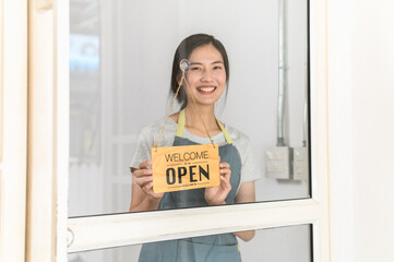 Smiling small business owner wearing apron holding open sign at shop entrance. Concept for entrepreneurship, startup, retail business, local store, service industry, and welcoming new customers.