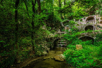 A small arched waterfall with a pool, by the old abandoned mill ruins in the forest near the...