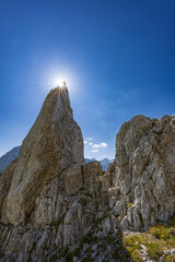 Dramatic view of Babe rock formation near Kamniško sedlo, Slovenia, with rugged alpine terrain, clear skies, and a scenic mountain hiking trail.