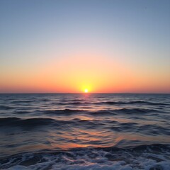 Fototapeta premium Vivid sunset illuminates the ocean waves with warm orange and yellow hues, creating a scenic coastal view.