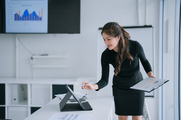 Businesswoman presenting financial charts on a digital tablet while holding a clipboard, analyzing data in a bright modern office for strategic planning, finance and collaboration