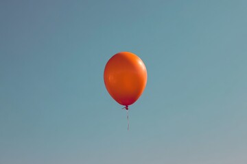 Fototapeta premium Orange balloon floats freely in air against clear blue background, creating a minimalist, simple atmosphere with clean lines and unattached, carefree aesthetic.