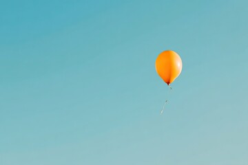 Obraz premium Orange balloon floats freely in air against clear blue background, creating a minimalist, simple atmosphere with clean lines and unattached, carefree aesthetic.