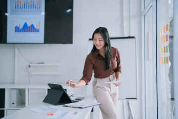 Asian businesswoman analyzing business data and charts in office, using a digital tablet with a stylus, demonstrating technology integration and professional work environment