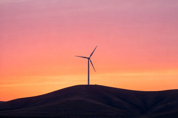 Wind turbine on a hill at sunset with vibrant orange and pink sky