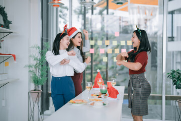 Three young Asian women wearing festive headwear are happily dancing and smiling during a Christmas...