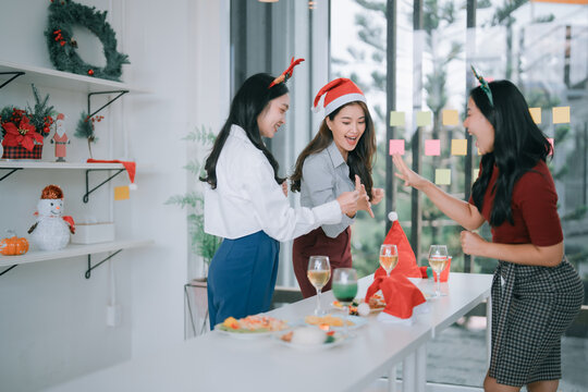 Young Asian women coworkers celebrating a festive Christmas holiday party in the office, having fun, laughing, and dancing together enjoying the food and drinks