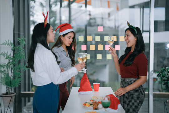 Three young Asian women colleagues are toasting with wine glasses while celebrating a Christmas office party, enjoying the festive atmosphere in their workplace