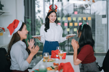 Asian businesswomen at an office Christmas party are happy, enjoying a festive celebration together with food and drinks, sharing a moment of joy wearing festive headwear