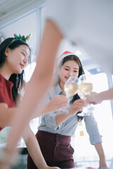Diverse group of smiling Asian women colleagues celebrate the festive season. Clinking champagne glasses in a joyful office during a Christmas party. Representing success. Teamwork. And holiday cheer