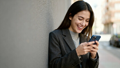 Happy laughing woman messaging on mobile phone. Young smiling business woman using smartphone on a city street. Concept for technology, communication, happiness, connection.