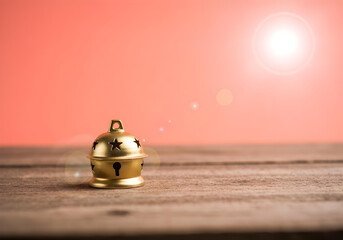 small golden christmas bell ornament on wooden surface with warm coral pink background and bokeh light effect