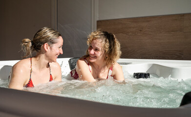 Two adult women enjoying a relaxing spa moment together in a hot tub during a weekend getaway, smiling and talking peacefully
