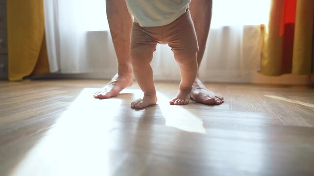 parent guides son. Proud father helps toddler take first step at home. Son taking first step with father support. Father assists son learn first step. Son first step milestone with supportive father.