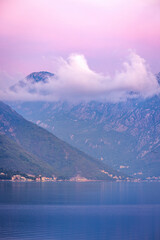 Calm pre-dawn over Kotor Bay, Montenegro, with misty mountains, soft clouds, and pink-blue sky reflecting in still waters before sunrise.