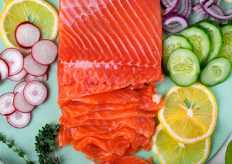 Salted trout fish fillet sliced on a green board, surrounded by chopped ingredients, vegetables and lemon, for making a salad. Healthy eating