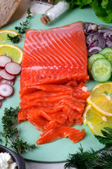 Salted trout fish fillet sliced on a green board, surrounded by chopped ingredients, vegetables and lemon, for making a salad. Healthy eating