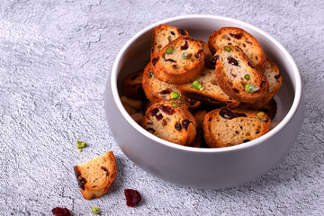 Rusks with dried cranberries and pistachios in ceramic bowl on light grey table