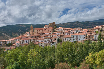 Fototapeta premium The charm of Linares de Mora, Aragon, a medieval village surrounded by mountains and dense vegetation under a dynamic sky