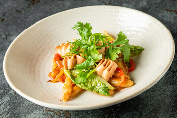 Stir-fried squid with snap peas and bell peppers, garnished with cilantro. Served on a ceramic plate over dark stone background. Colorful Asian seafood dish, top view
