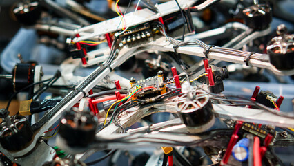 Fototapeta premium Close-up of disassembled quadcopter frames with wires, ESCs and brushless motors, centered on a flight controller in a workshop repair scene. Photo