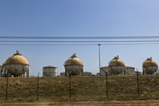 A view of large, spherical oil or gas storage tanks with the letters "CLC" on them, set against a clear blue sky. A fence and power lines are visible in the foreground.