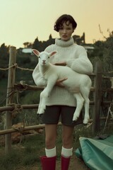 Young person holding a white lamb in a green field during sunset in a rural setting