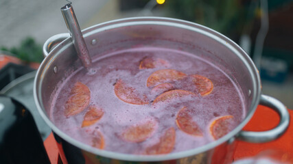 A close-up of hot mulled wine being prepared in a large metal pot. The brewing process of this traditional winter drink. Image used to illustrate recipes, Christmas traditions, and winter treats.